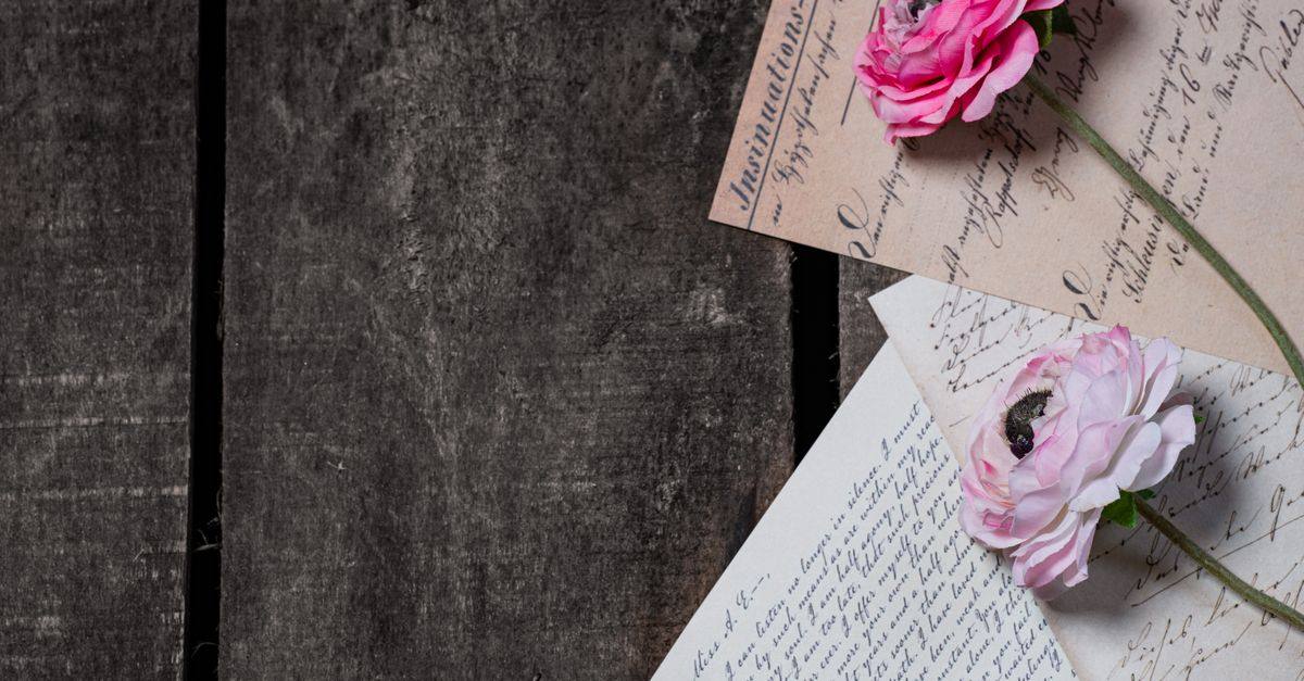 Pink roses rest on vintage handwritten letters on a dark tabletop.