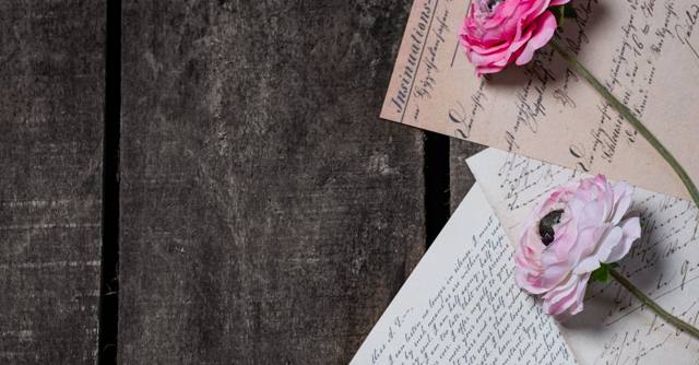 Pink roses rest on vintage handwritten letters on a dark tabletop.