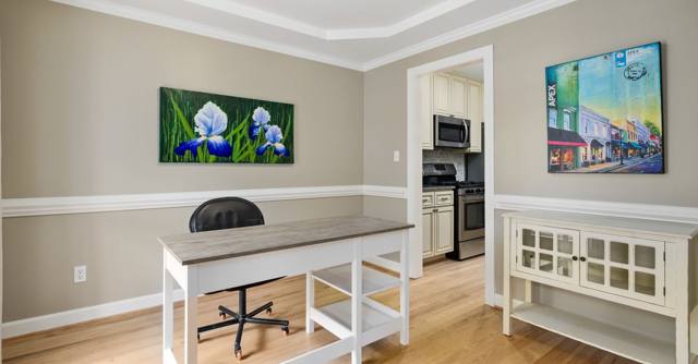 A bright home office with colorful paintings on neutral walls.