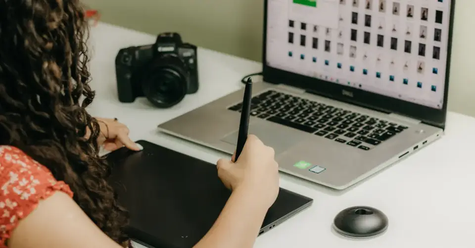A woman uses a graphics tablet while reviewing photographs on a laptop.
