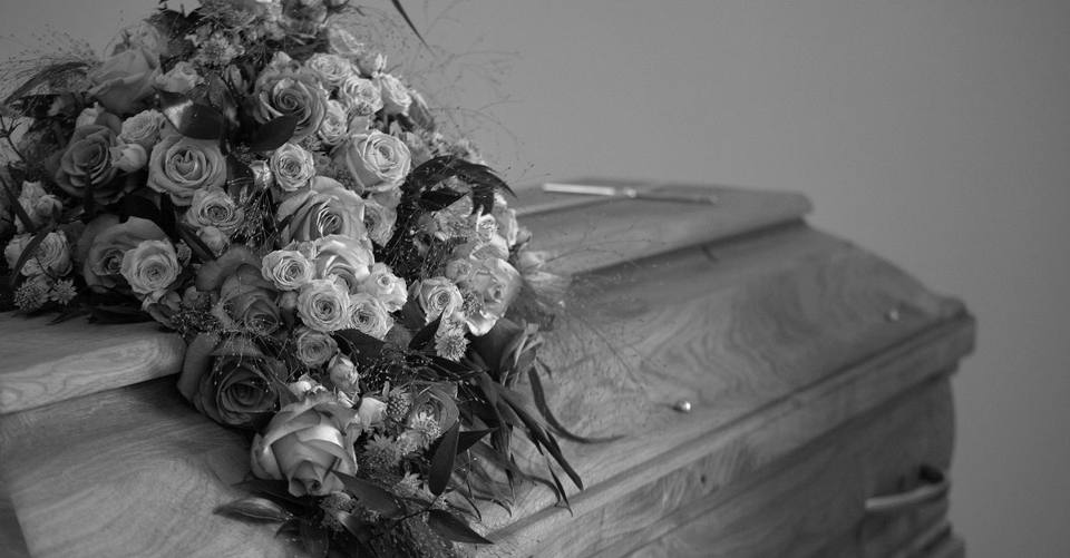 A black and white image featuring a wooden casket adorned with a vibrant floral bouquet, symbolizing respect and memory.