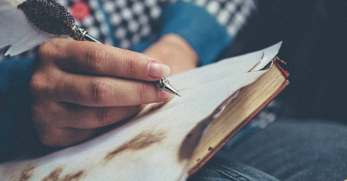 Close-up of a person using a quill pen to write in a vintage notebook.
