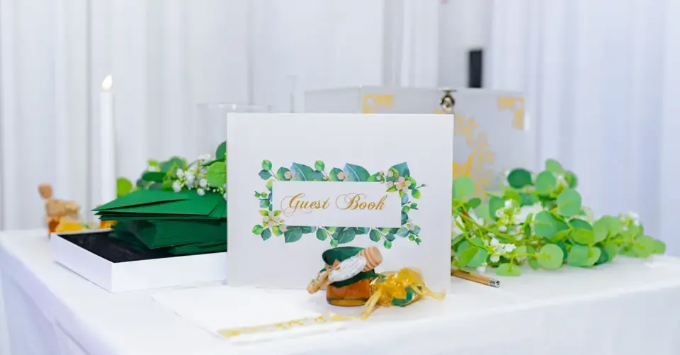 A floral wedding guest book display sits beside green favor boxes and a candle.