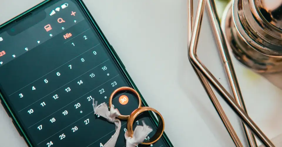 Two wedding rings rest on a smartphone displaying a calendar.