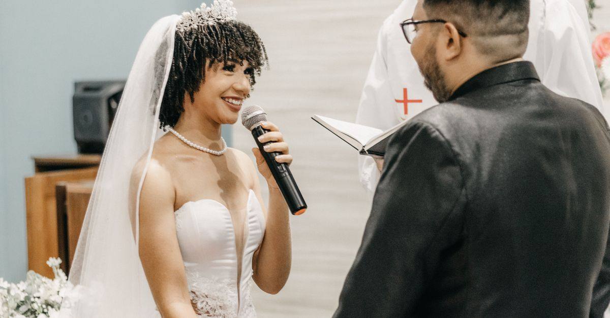 A bride speaks into a microphone while exchanging vows with her partner.