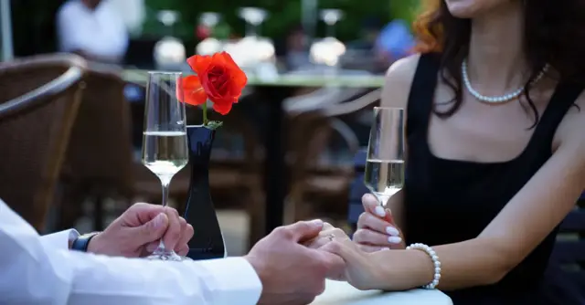 A couple enjoying a romantic dinner with champagne and a red rose centerpiece in a restaurant.