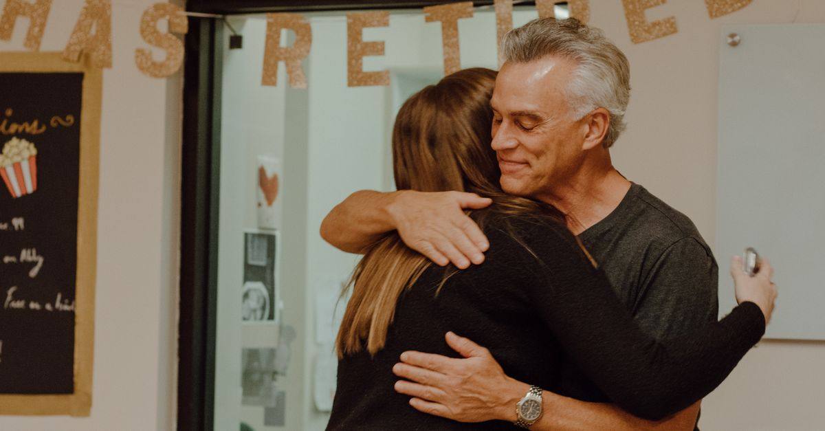 A heartfelt moment as two people embrace at a retirement party with festive decor.