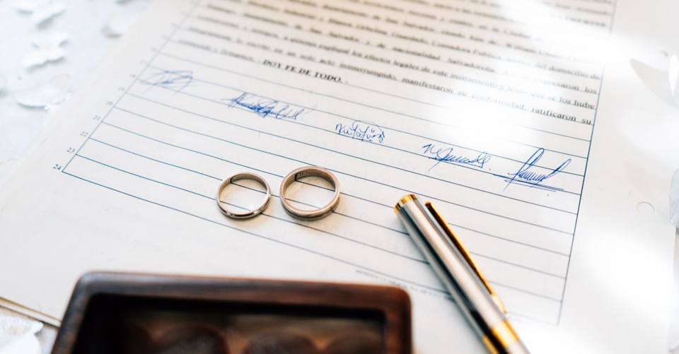 Two wedding rings rest on a signed marriage certificate beside a gold pen.