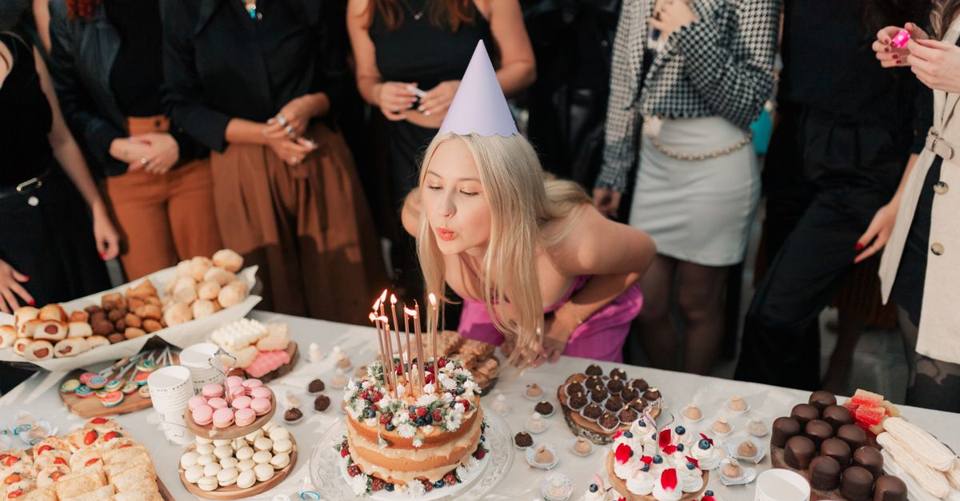 A cheerful young woman celebrates her birthday, surrounded by friends and a variety of delicious cakes and desserts.