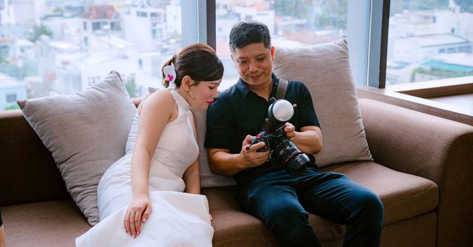 A newlywed couple sit on a sofa and review wedding photos on a camera.