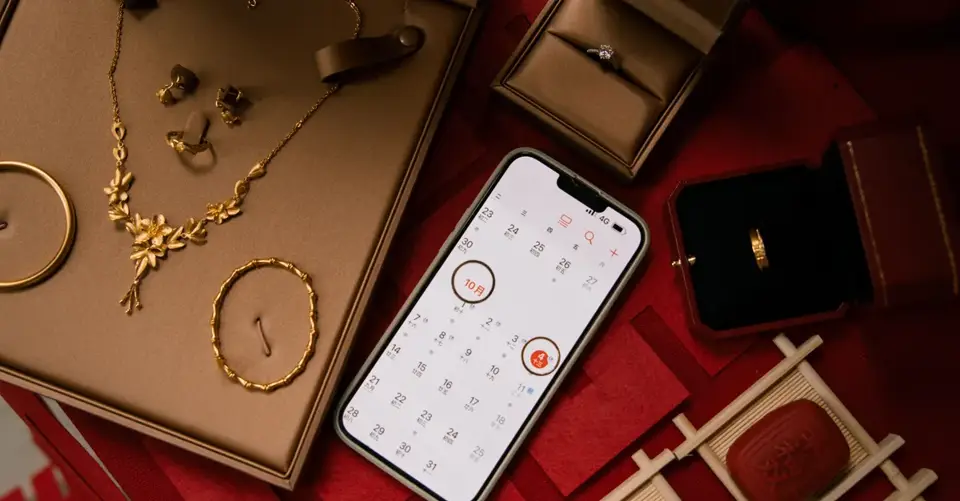 A smartphone calendar lies among jewelry and gift boxes on a red tabletop.