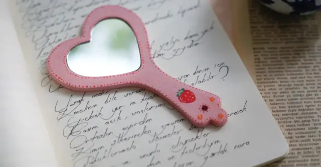 A pink heart-shaped mirror on handwritten pages, invoking romance and nostalgia.