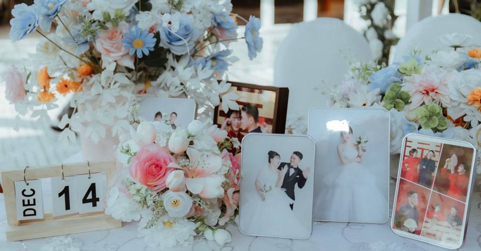 Framed wedding photographs stand among blue-and-white flowers on a decorated table.