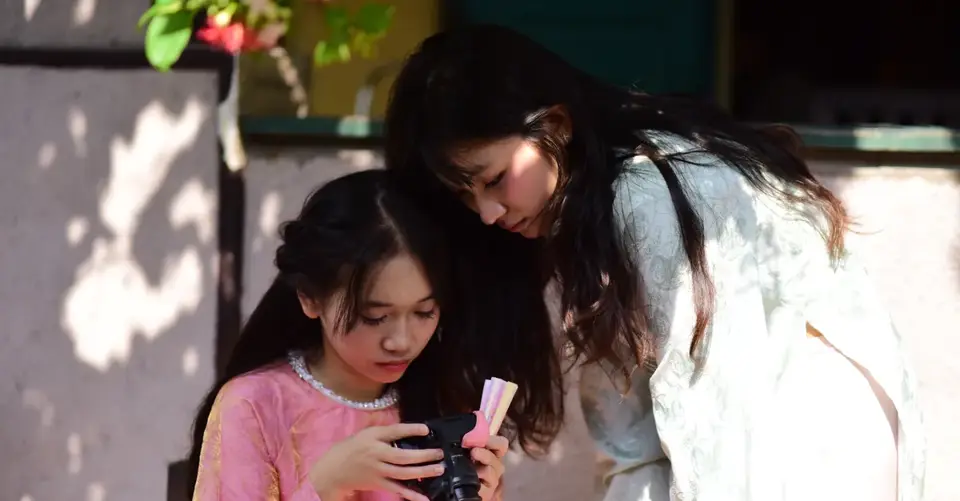 A mother and daughter look together at photos on a digital camera outdoors.