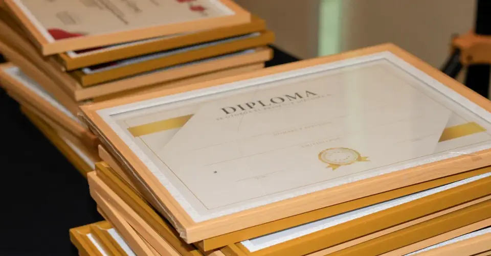 Several framed diplomas are stacked on a table before an academic ceremony.