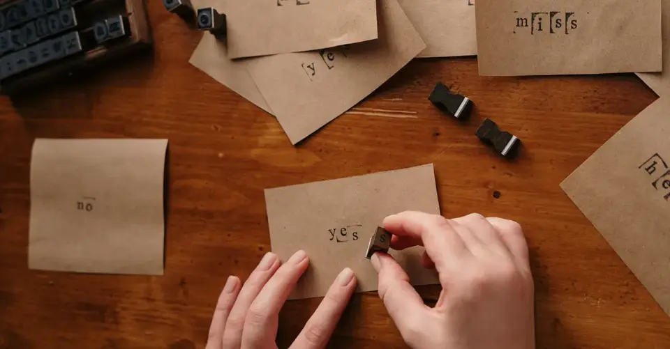 Hands arrange vintage letterpress stamps on small kraft-paper cards.