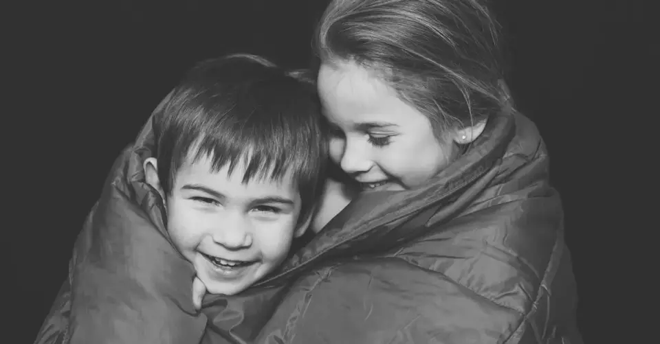 Two happy caucasian children wrapped in a warm blanket sharing a joyful moment indoors.