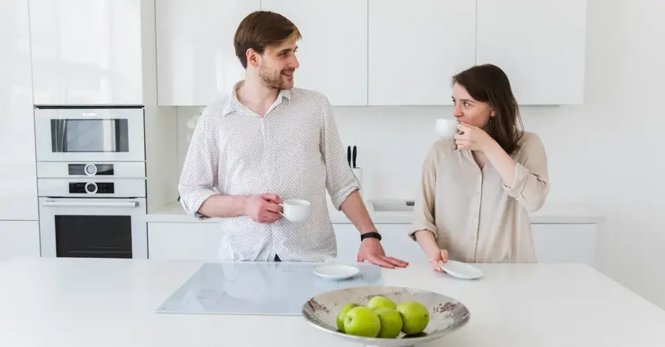 A couple share coffee and conversation across a bright white kitchen counter.