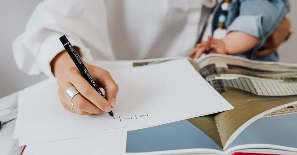 A mother writes in a notebook while holding her baby on her lap.
