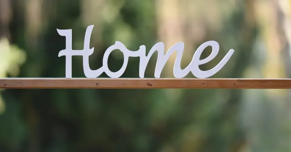 Elegant wooden 'Home' sign against a blurred green background, perfect for cozy decor themes.