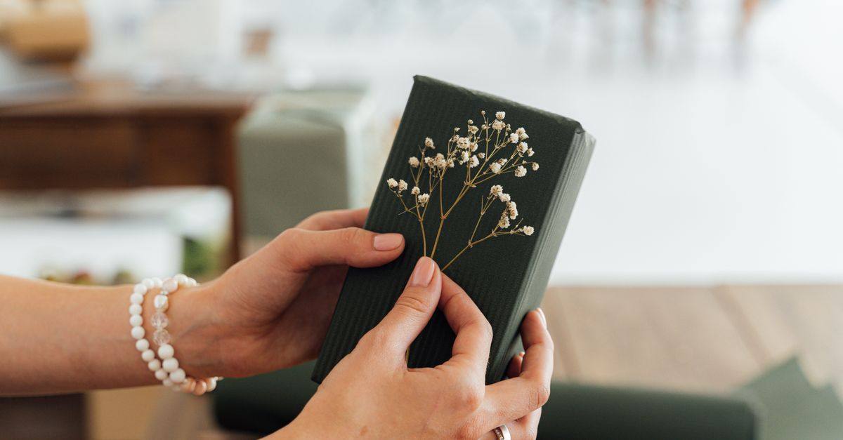 Hands hold a dark green gift decorated with small white flowers.