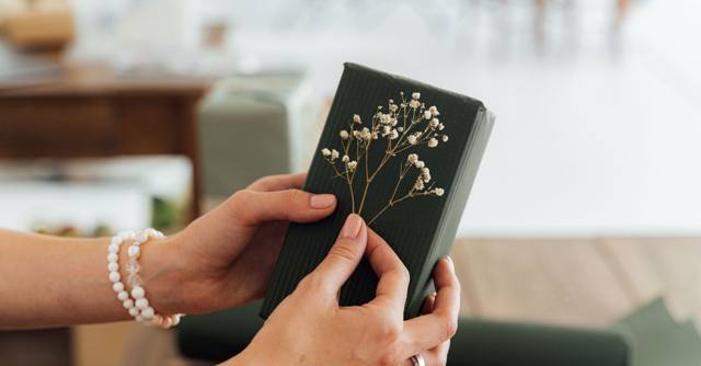 Hands hold a dark green gift decorated with small white flowers.
