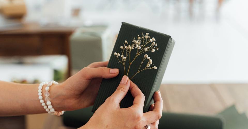 Hands hold a dark green gift decorated with small white flowers.