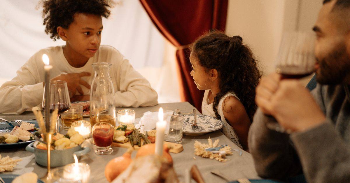 A family talks around a candlelit holiday dinner table.