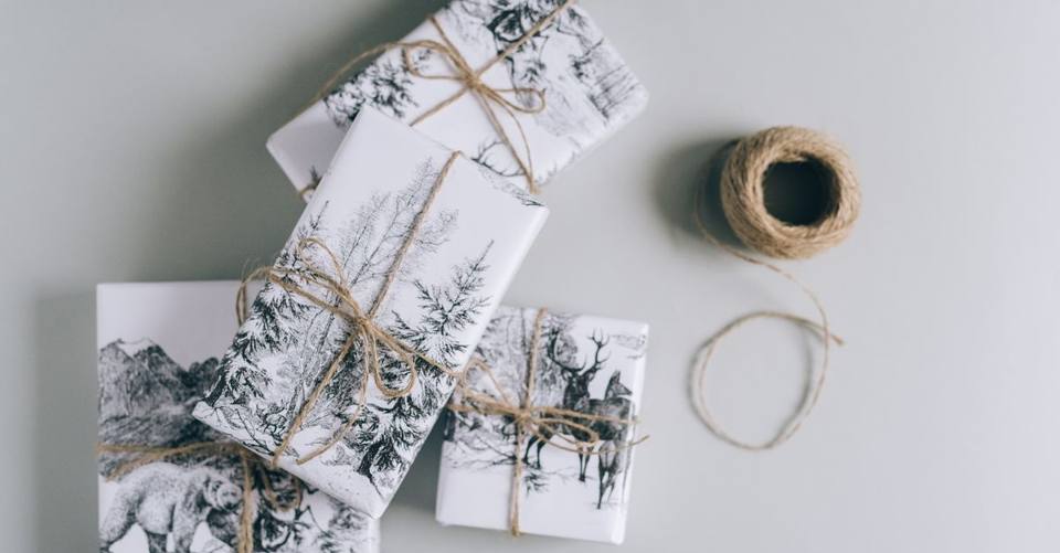 Several small gifts wrapped in illustrated paper and twine sit on a pale table.