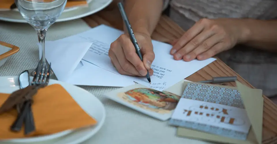 A person writes a thank-you note at a Thanksgiving table set with a plate and glassware.