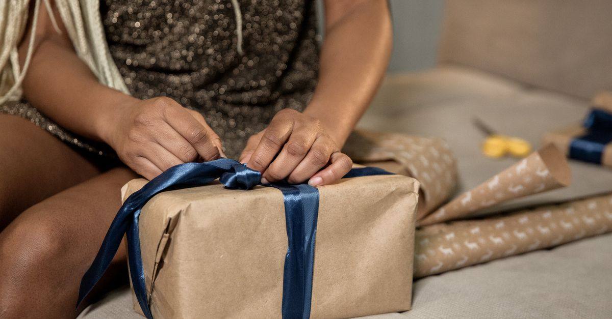 Hands tie a blue ribbon around a gift wrapped in brown paper.