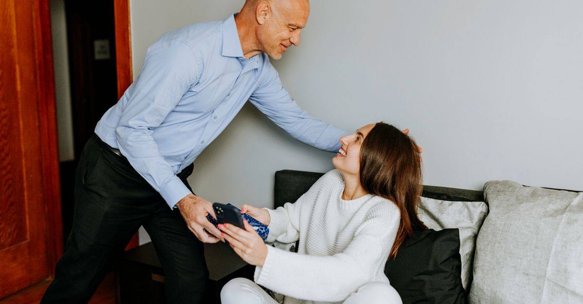 A father gives his adult daughter a gift as they sit together at home.