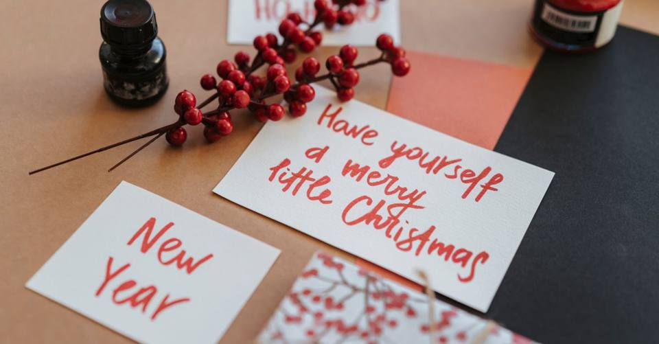 Handwritten Christmas and New Year cards sit among red berries, ink, and paper.