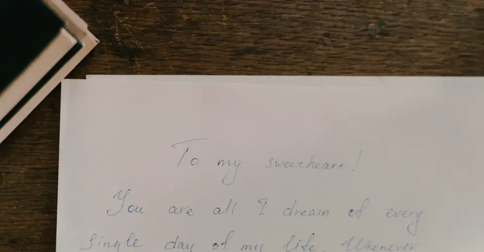 A handwritten love letter lies open on a wooden table beside a laptop.