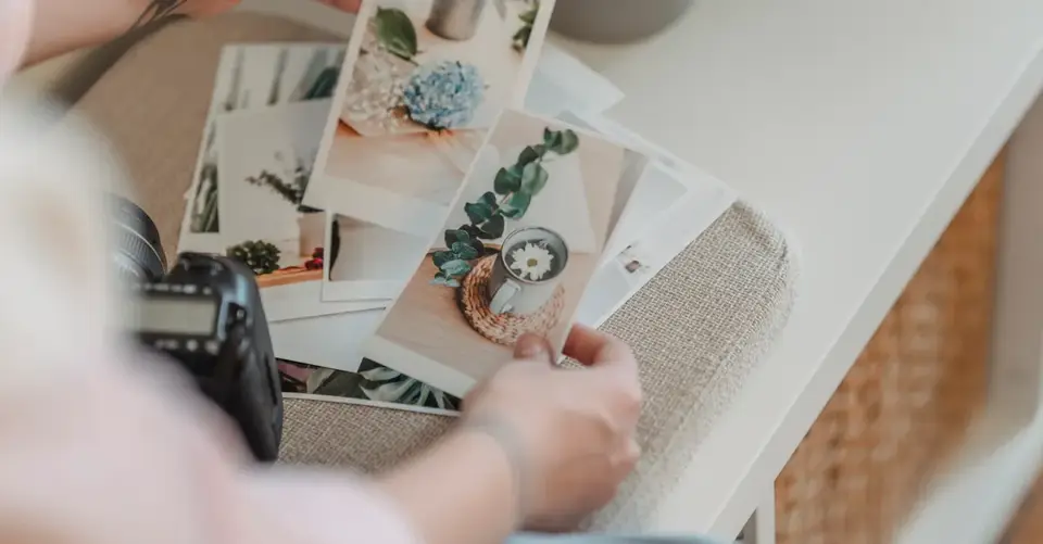 A person reviews a spread of printed photographs on a white table.