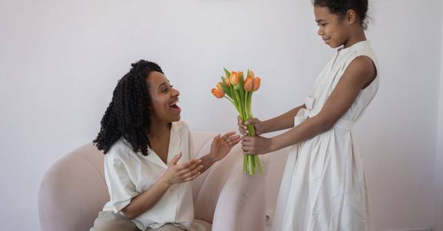 A daughter gives her mother a bouquet of orange tulips at home.