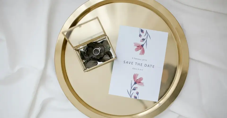 A save-the-date card and engagement ring rest on a round gold tray.