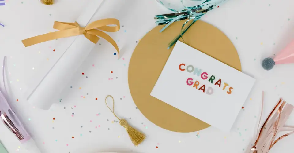 A “Congrats Grad” card, tassel, ribbon, and confetti form a graduation flat lay.
