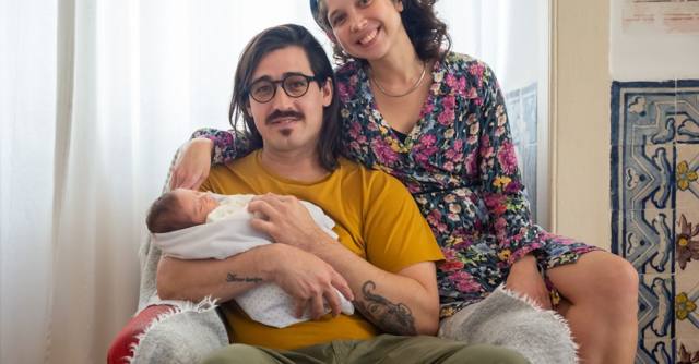 Two parents sit at home with their newborn baby.