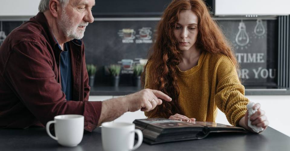 An older man and adult daughter sit together and look through a photo album.