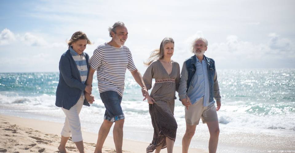 Happy senior couples walking along a sunny Portuguese beach, enjoying a leisurely day by the sea.