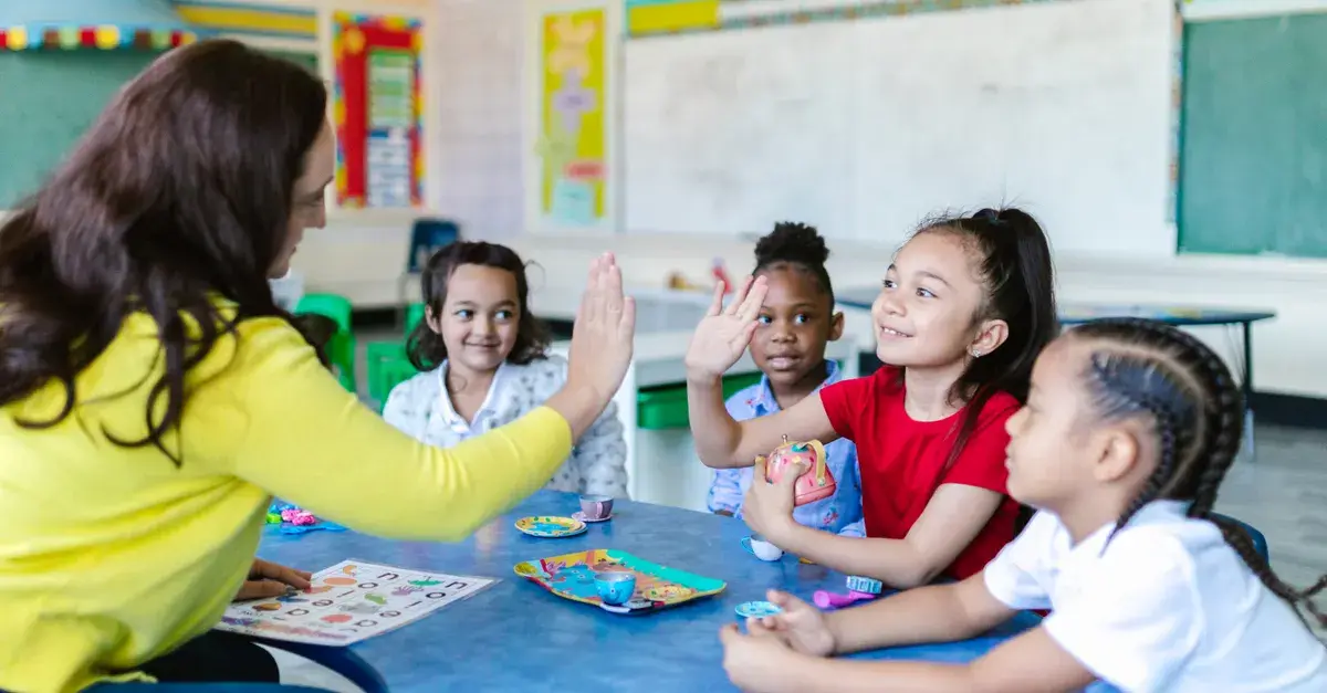 Teacher and diverse students high-five in a lively classroom setting.