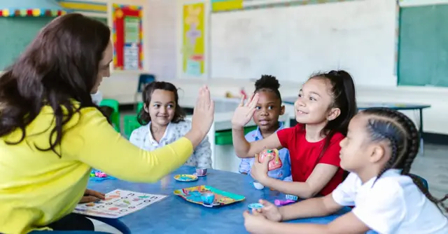 Teacher and diverse students high-five in a lively classroom setting.