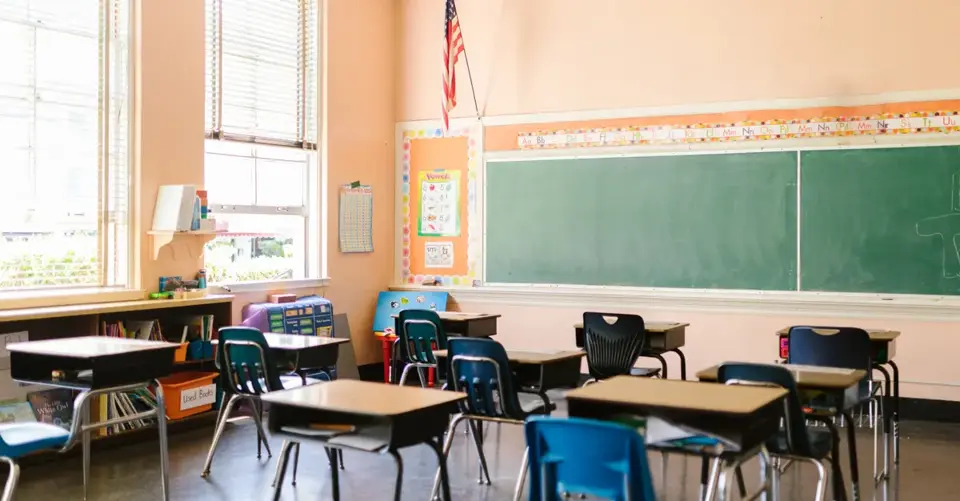 An inviting, sunlit classroom with empty desks and an American flag, ready for students.