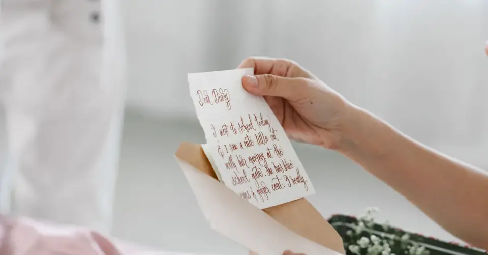 Hands lift a handwritten letter from a kraft-paper envelope.