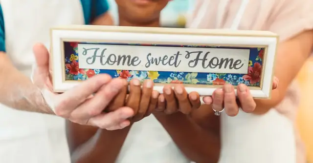 Close-up of a family holding a 'Home Sweet Home' sign, symbolizing warmth and togetherness.