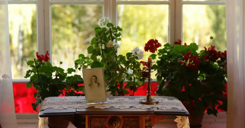A framed portrait, flowers, and a candle create a quiet memorial display by a sunny window.
